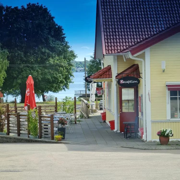 En bild på Evedals Camping som visar en mysig stuga omgiven av lummiga skuggor. Utomhusmöbler står placerade i närheten, vilket ger en inbjudande känsla för besökare.