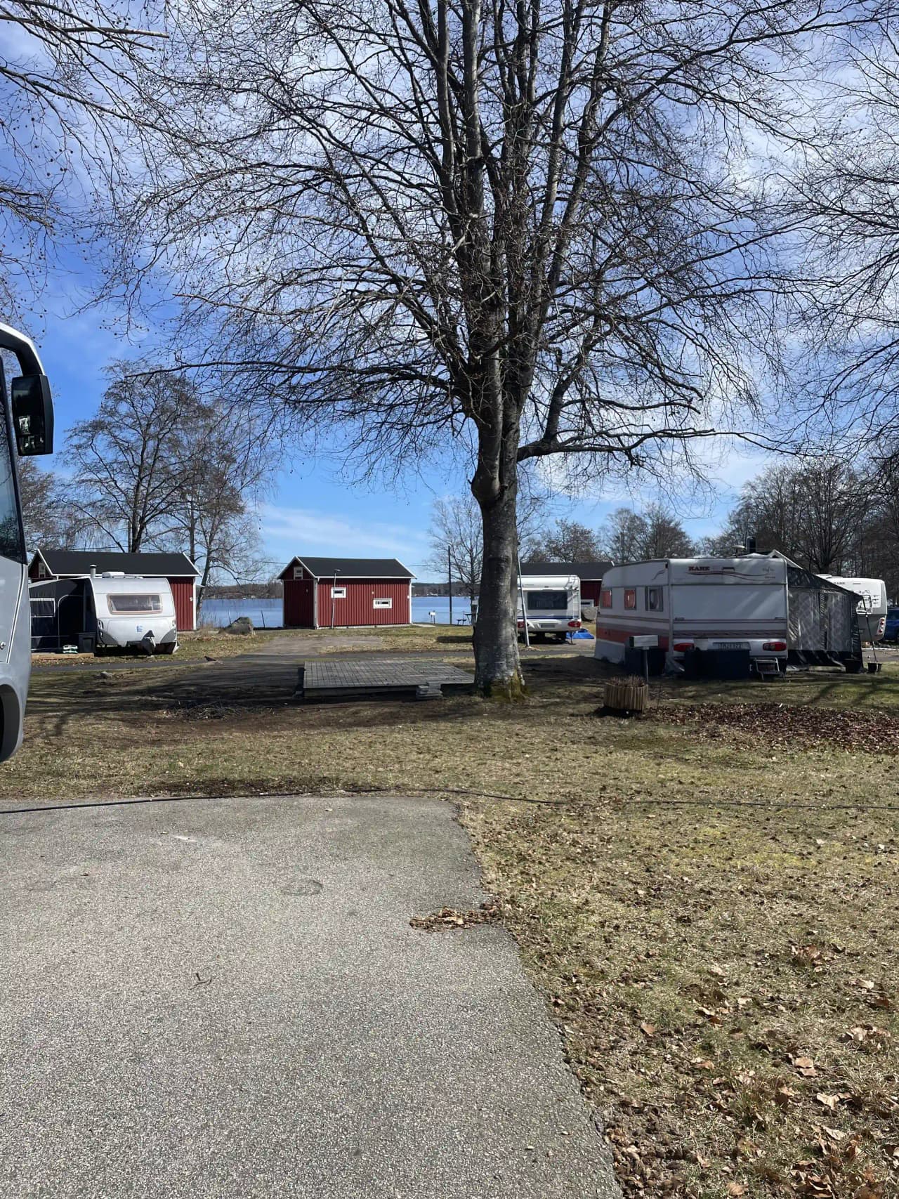 En campingplats med olika typer av husbilar och husvagnar parkerade längs en grusväg. En semi-trailer truck och en skåpbil syns även i bakgrunden, omgivna av grönska.