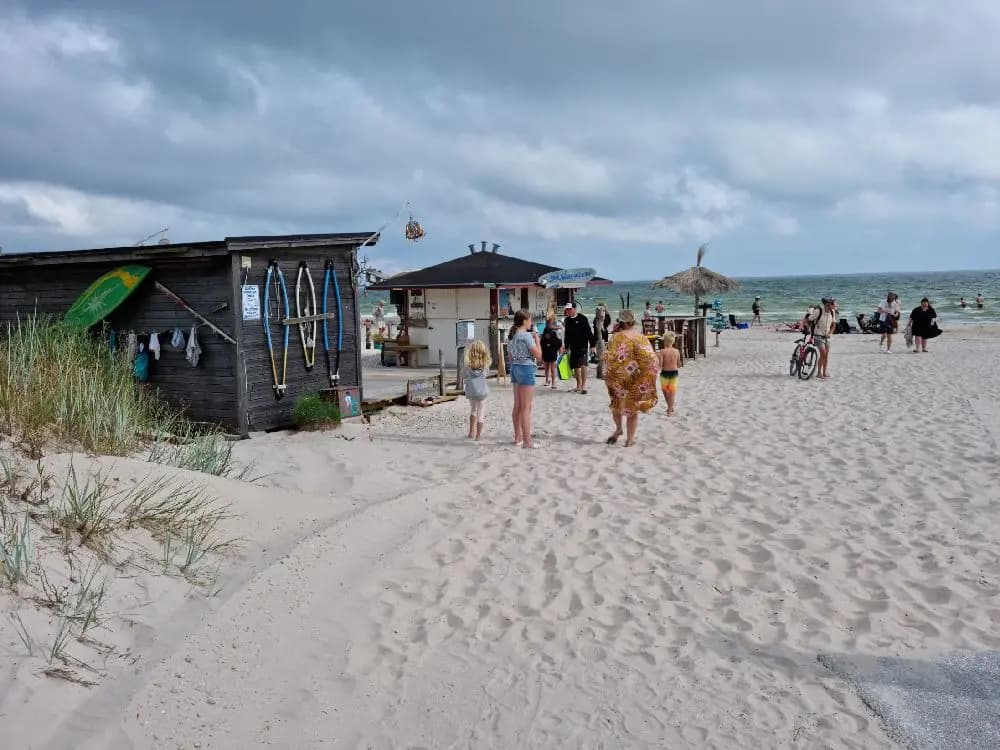 En solig sommardag på Sudersand Resort, med semesterfirare som njuter av stranden, sanden och havet. Parasoll ger skugga åt de badande.