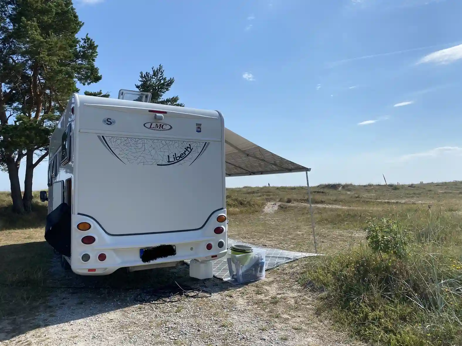 En rad av husvagnar och husbilar som står parkerade på en campingplats vid Sudersand Resort, omgivna av grönskande natur och en klar himmel.