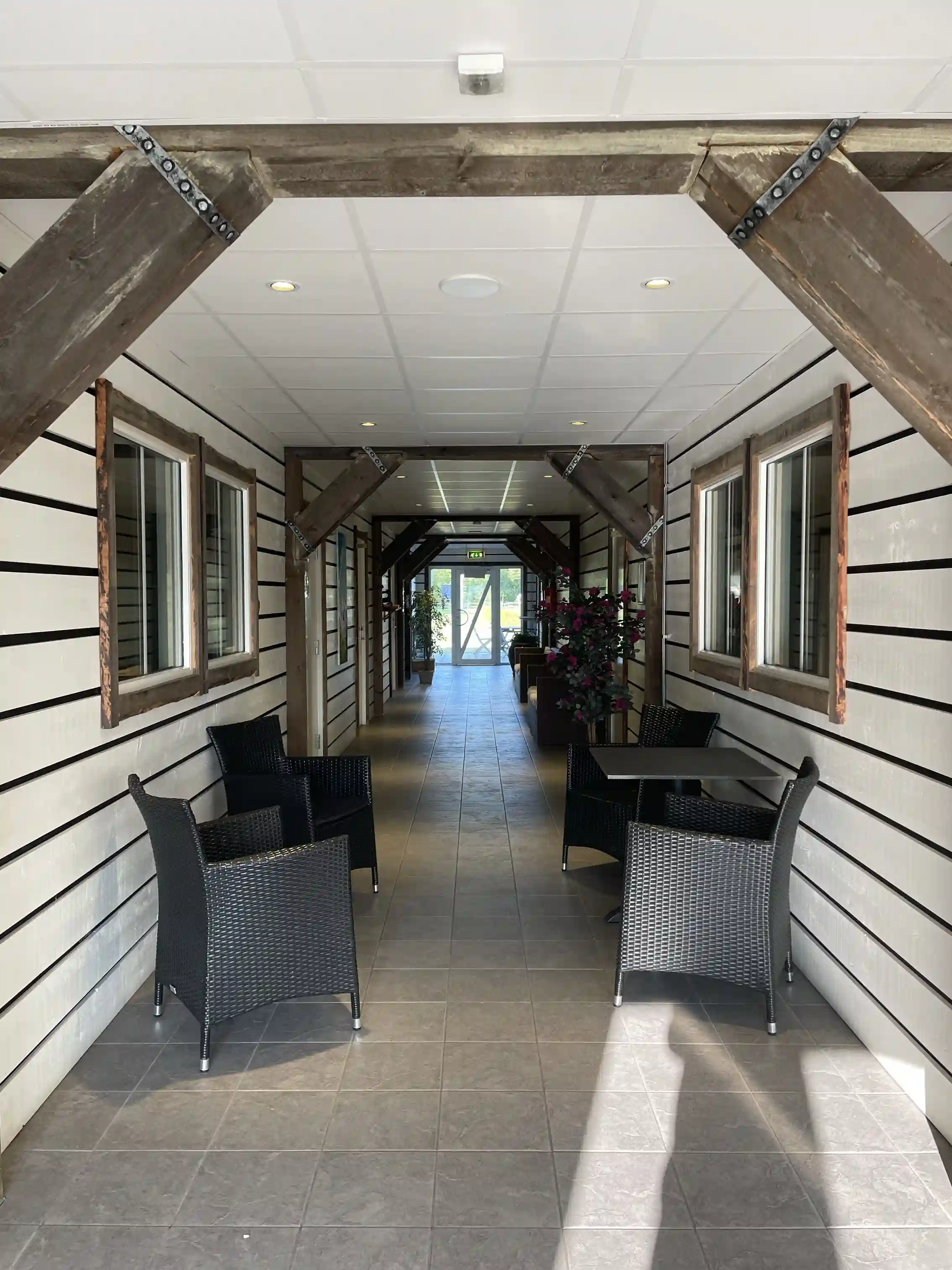 En interiörbild av en träbyggnad vid Sudersand Resort, med synliga takbjälkar och plankor, samt en dörr och element av stål som kompletterar den rustika trädesignen.