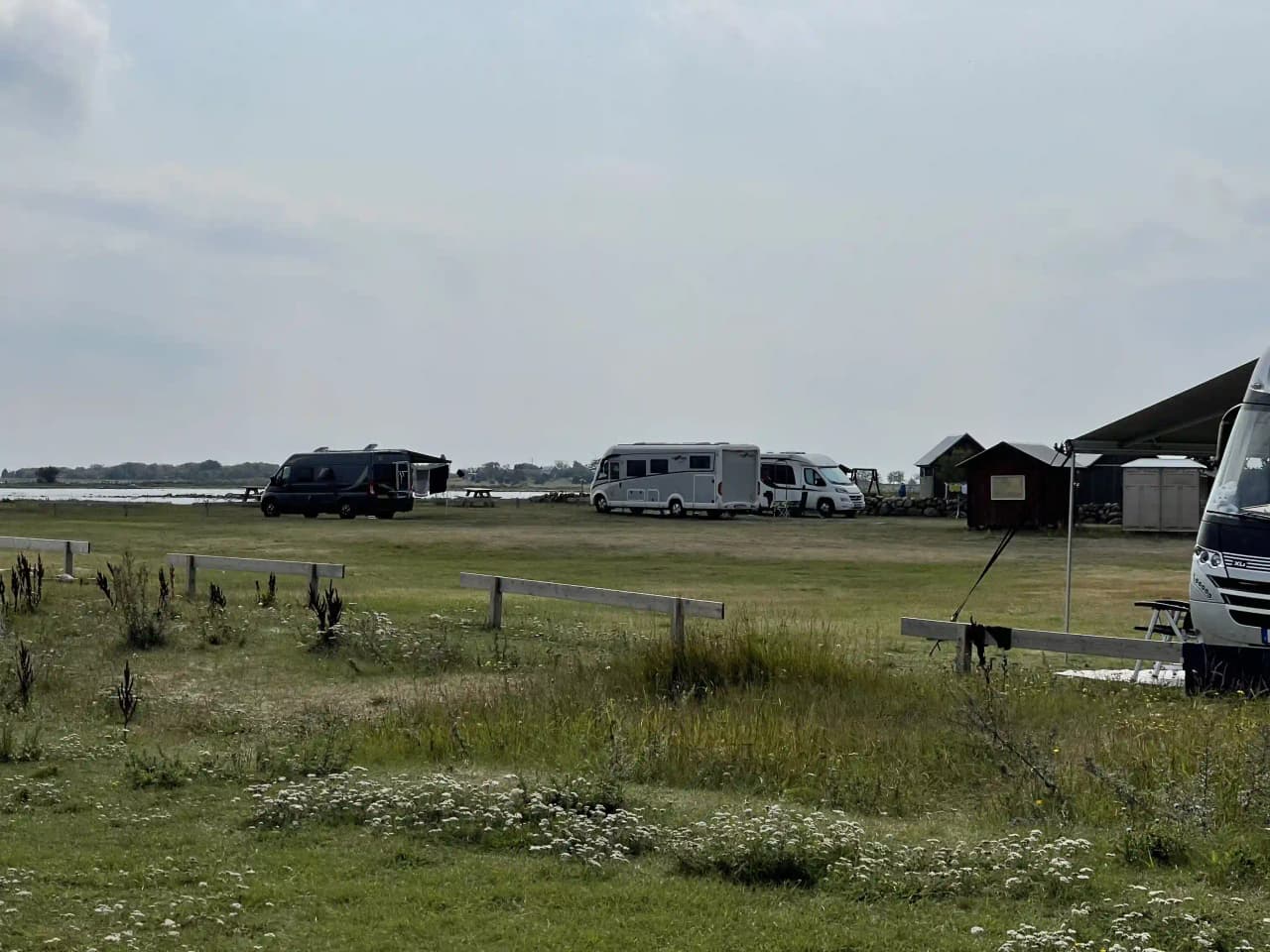 Bild av Wikegårds semesterby & ställplatscamping som visar flera husbilar och husvagnar parkerade på en öppen plats. I bakgrunden syns öppna fält och himlen.