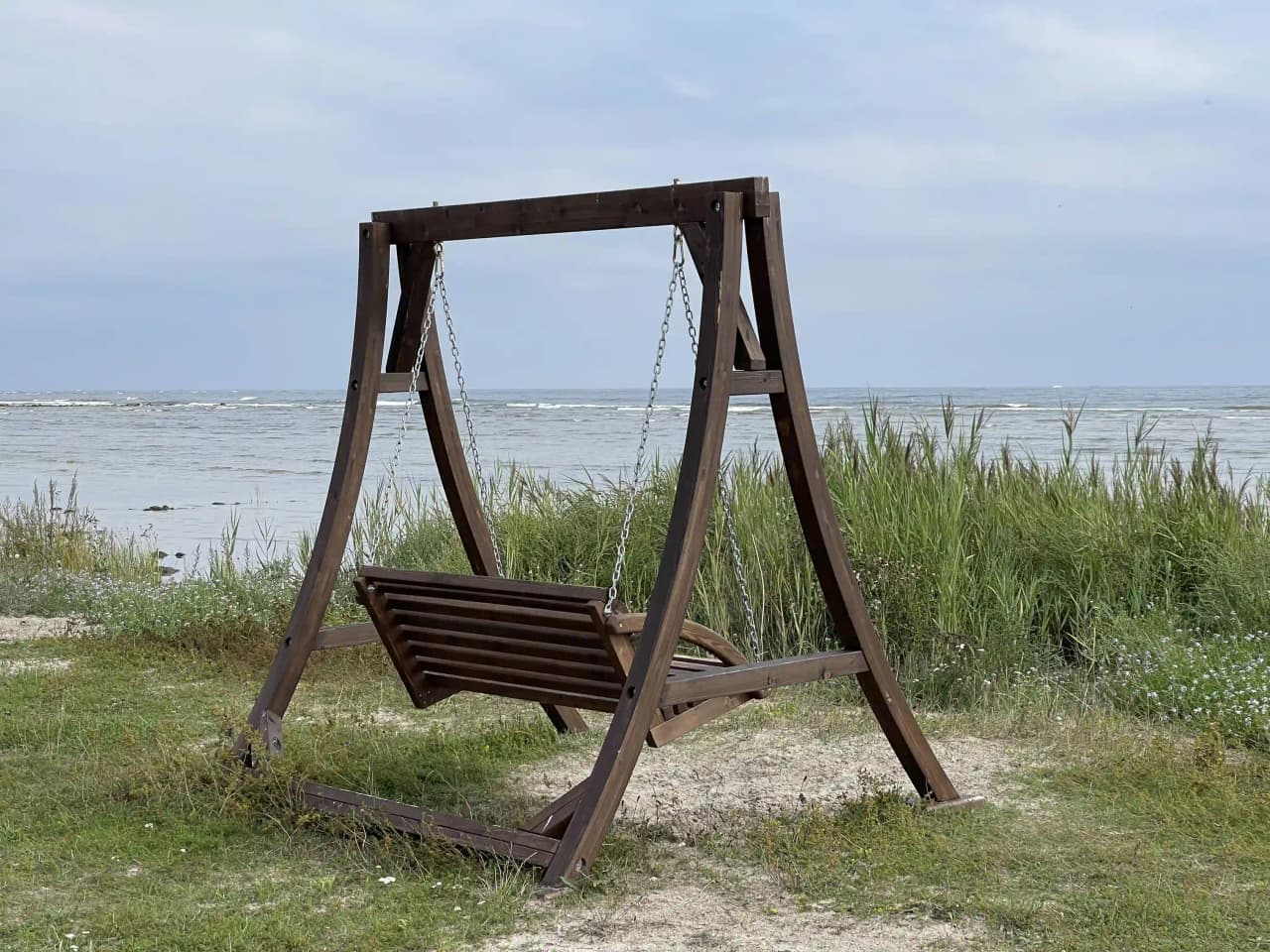 Bild av Wikegårds Semesterby & Ställplatscamping med trälandskap och kustlinje i bakgrunden. Morgonljuset skiner över en enkel utemöbel placerad på grässlätten nära stranden.