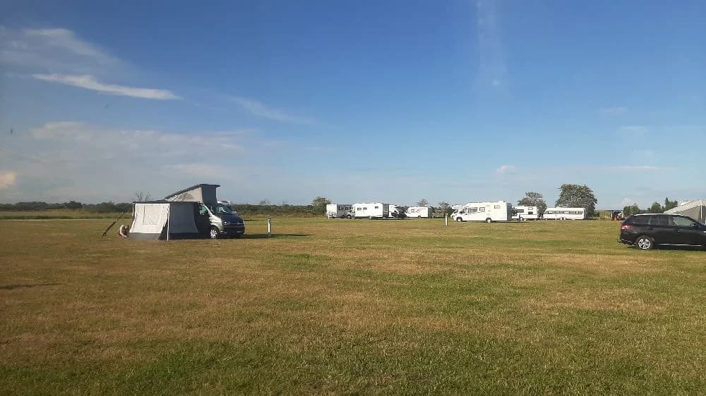 En vidsträckt grässlätt under en klarblå himmel med några vita moln. Området ser ut att vara en fridfull plats, perfekt för utomhusaktiviteter.
