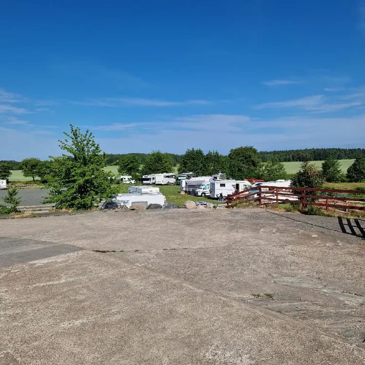 En ställplats vid Kedumsvik med husbilar och husvagnar parkerade på ett öppet område under en molnig himmel.
