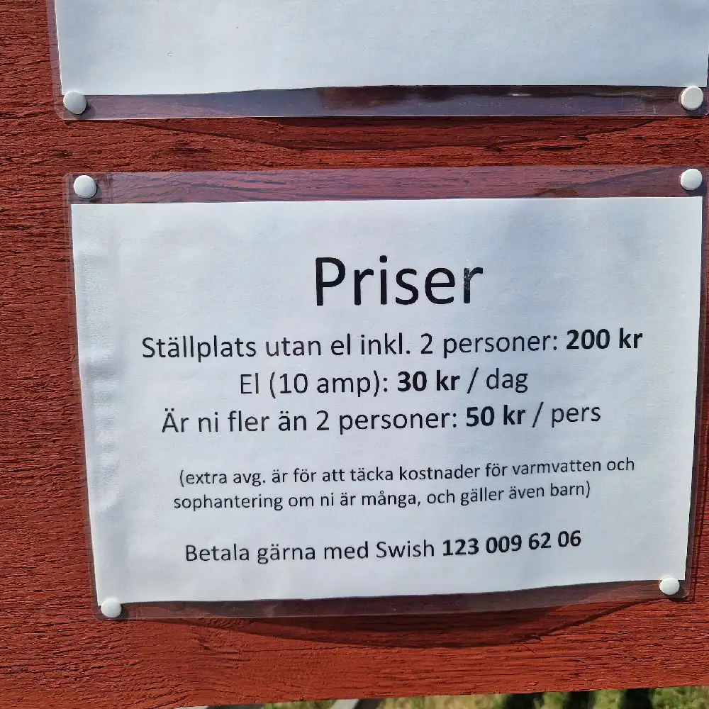 En skylt i trä med brun nyans vid Kedumsvik ställplats, med enkel text ingraverad på ytan. Skylten är gjord av plank och plywood, och den står som vägledning för besökare på platsen.