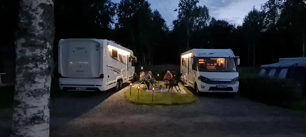 En campingplats med flera husvagnar och husbilar uppställda på en grusplan, omgiven av grönska och träd.