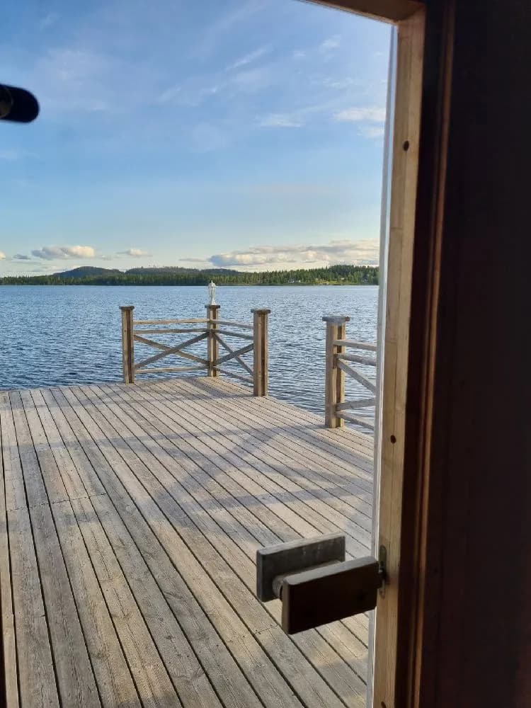 En träbrygga sträcker sig ut över en stilla sjö vid Kolgårdens stugby & camping, omgiven av frodiga skogar.