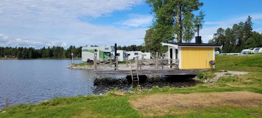 En naturskön vy över ett sjölandskap vid Kolgårdens stugby & camping, med stilla vatten omgiven av grönska och mobila hem som ger en avkopplande och rofylld atmosfär.