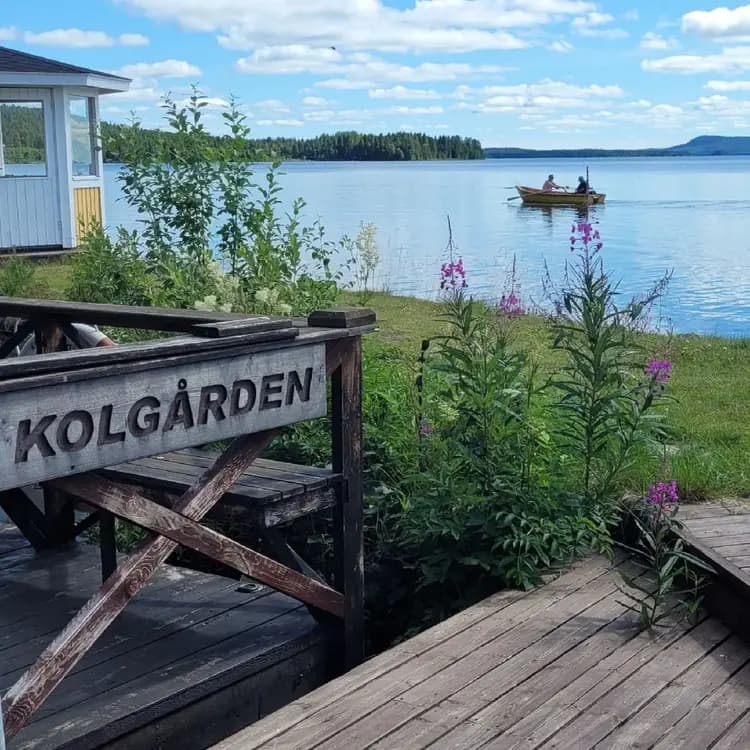 En pittoresk stuga med utomhusborden nära en brygga vid en sjö omgiven av grönska. Perfekt för besökare som söker naturupplevelser och avkopplande stunder vid en ekovänlig stugby.