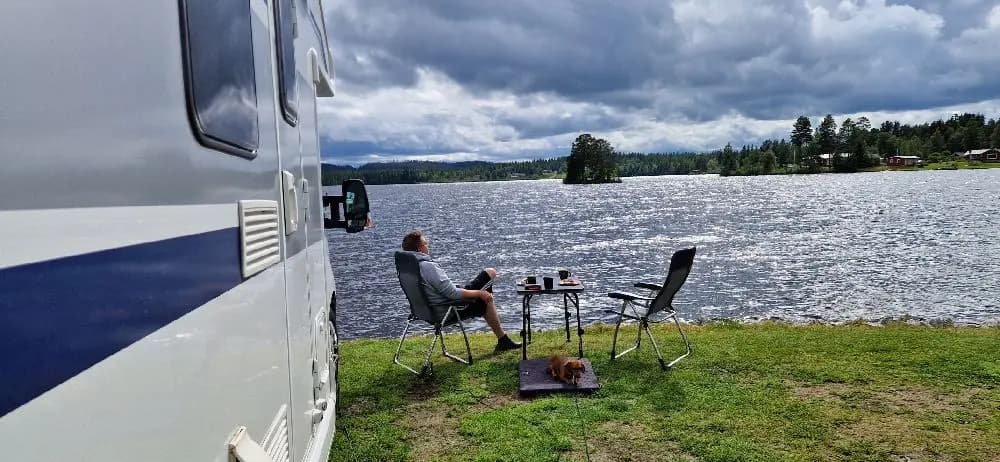 En husvagn står parkerad vid en sjö omgiven av grönskande natur, sannolikt inom Kolgårdens stugby & camping.