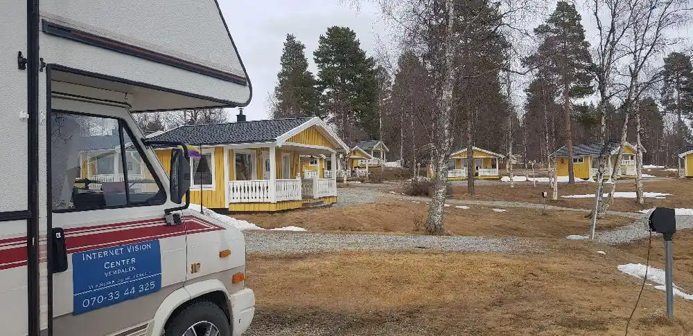 En mysig stuga på Kolgårdens stugby & camping med en charmig trädgård, en uppfart och en husbil parkerad utanför.