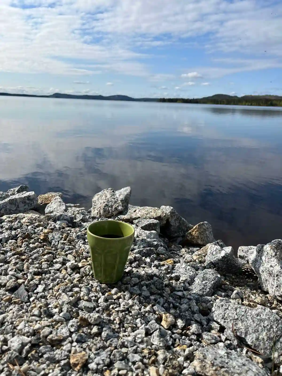 En naturskön vy vid Kolgårdens stugby & camping med en blå sjö omgiven av klippiga kustlandskap och småstenar längs stranden.