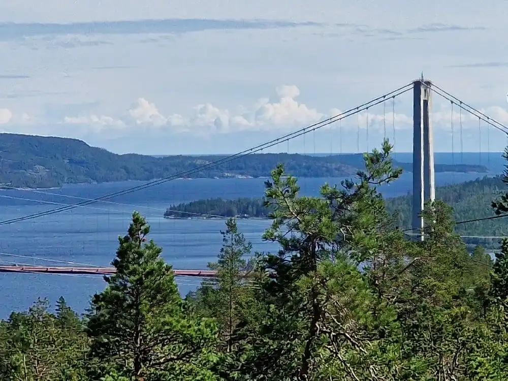 En kabelhängbro över ett vatten med omgivande kustlandskap, belägen nära Snibbens camping.
