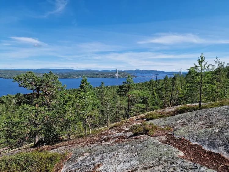 Vy över Snibbens camping med blå himmel i bakgrunden. Grönskande växtlighet omger området, vilket ligger inbäddat i ett naturskönt landskap med kullar och havsrelaterade formationer.