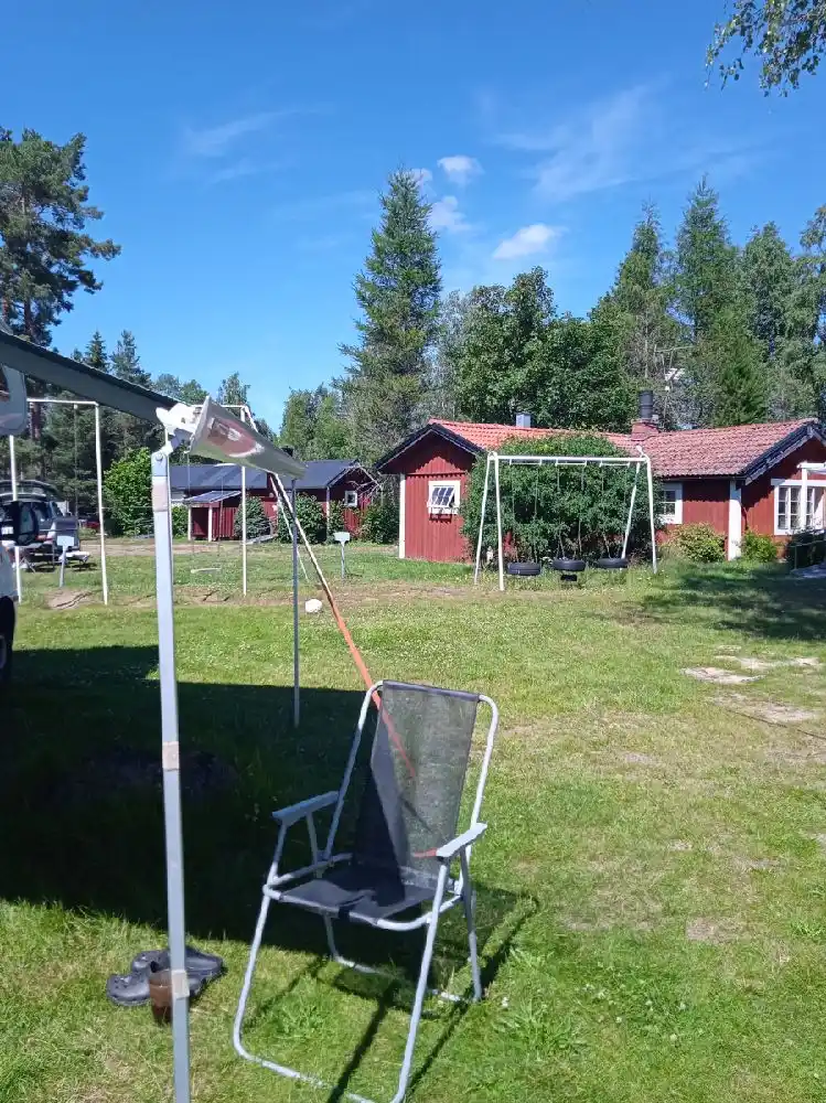 En grön gräsmatta med trädgårdsmöbler, inklusive vikstolar, står i skuggan vid Lesjöbyns camping, som ger en inbjudande och avkopplande atmosfär för besökare.