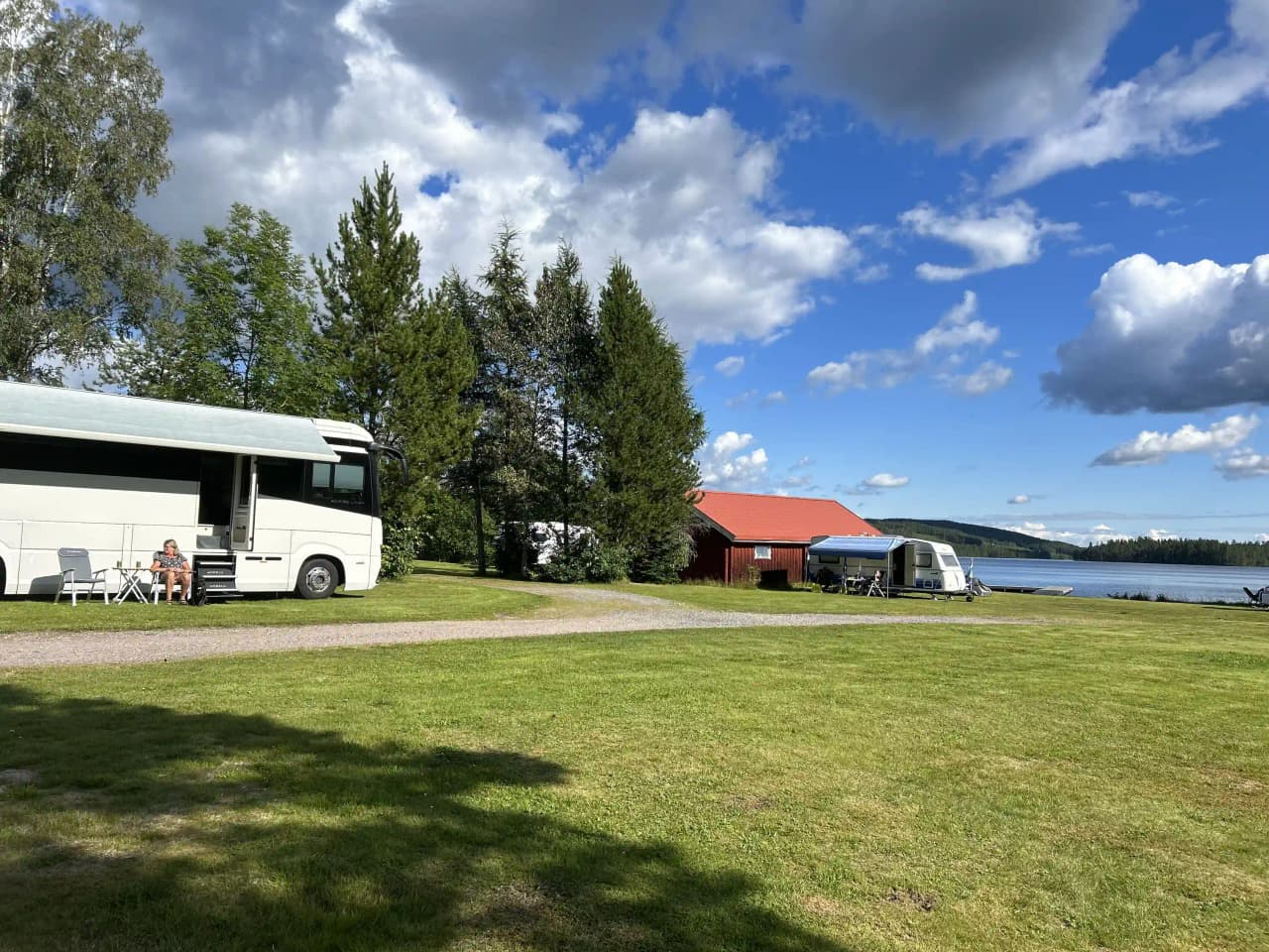 En campingplats vid en sjö med ett tält bredvid en husbil under molnig himmel i Lesjöbyns campingområde.