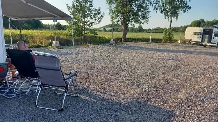 En bild av en parkering vid södra Kinda båtklubb med flera husbilar och skåpbilar uppställda längs en uppfart. Vegetation syns i bakgrunden, vilket skapar en lugn och naturnära atmosfär.