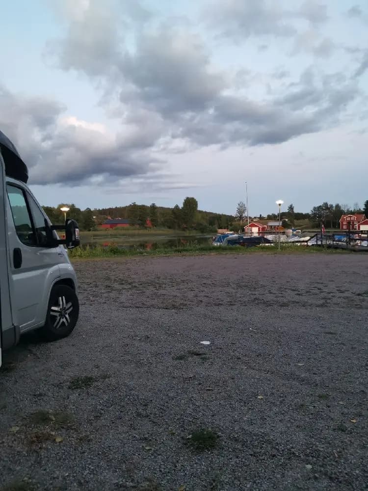 En bil står parkerad vid en sjö under en molnig himmel, troligen vid Södra Kinda Båtklubb.