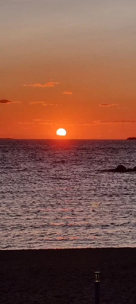 En solnedgång över en vattenyta vid Askeviks camping & stugor, med himlen i orange och röda nyanser, där horisonten möter vattnet i en lugn och stillsam atmosfär.