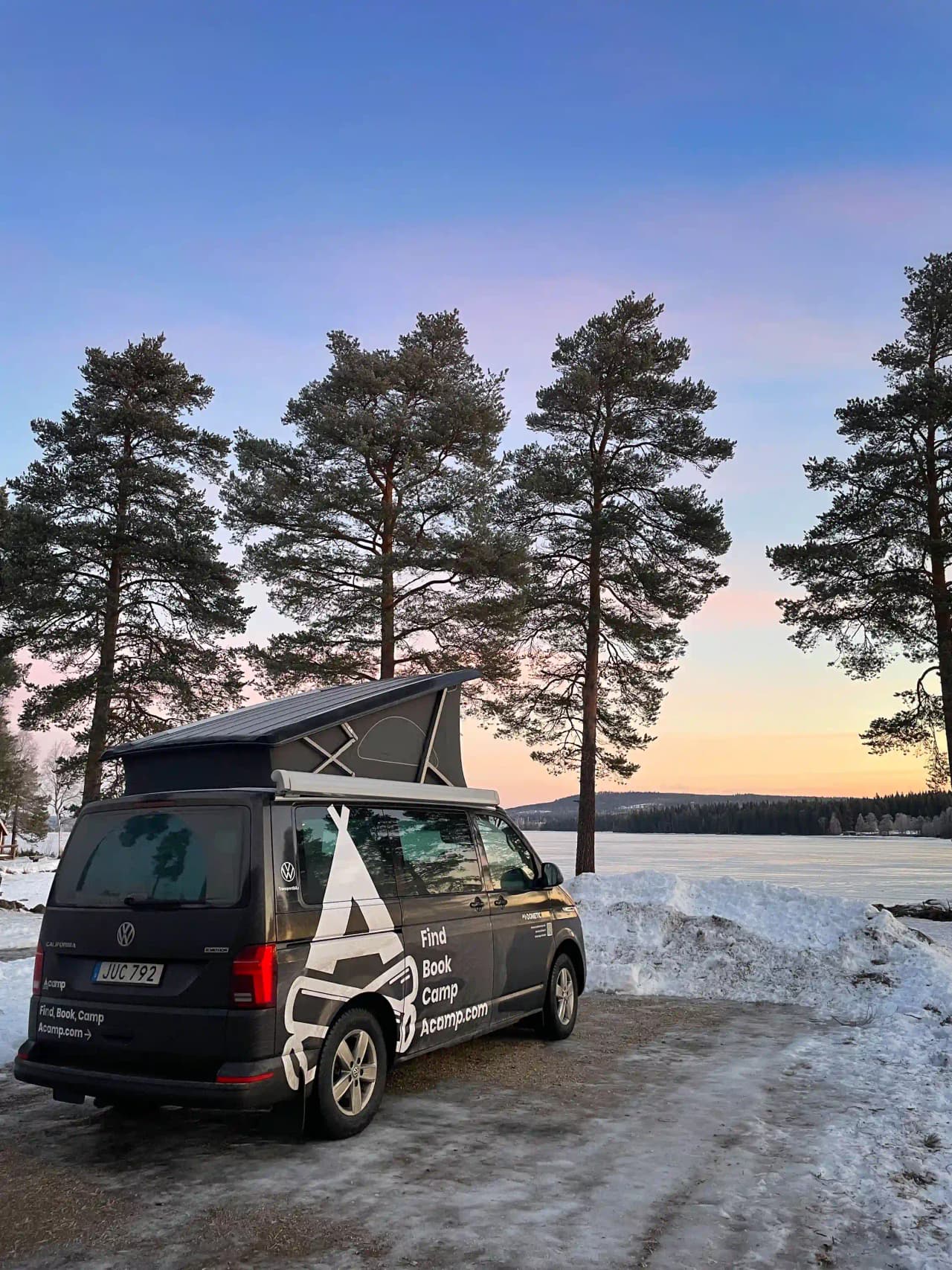 En vit Volkswagen skåpbil står parkerad på en grusväg vid Camp Viking, med natur i bakgrunden.