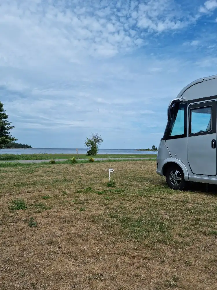 En campingplats med husbilar och husvagnar uppställda på en grön gräsyta under en klarblå himmel.