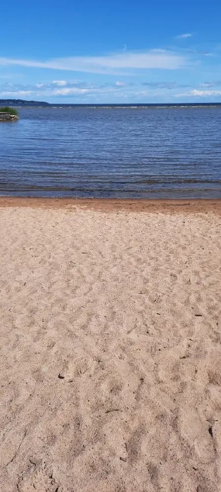 En sandstrand vid ett blåskimrande hav under en klar horisont, omgiven av kustlandskap.