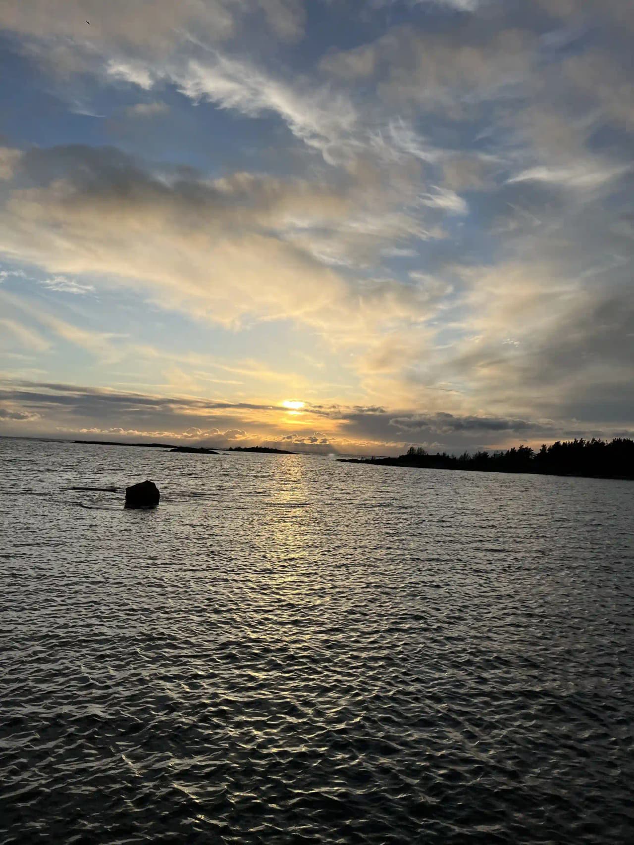 En lugn vattenyta med en vid horisont under en blå himmel med lätt molnighet vid Filsbäcks camping.