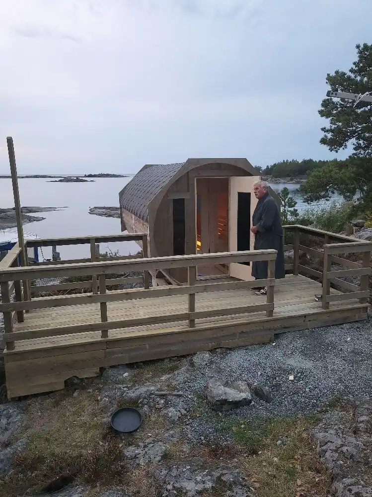 En träbrygga med en liten stuga eller skjul i bakgrunden på Filsbäcks camping, omgiven av grönskande natur.