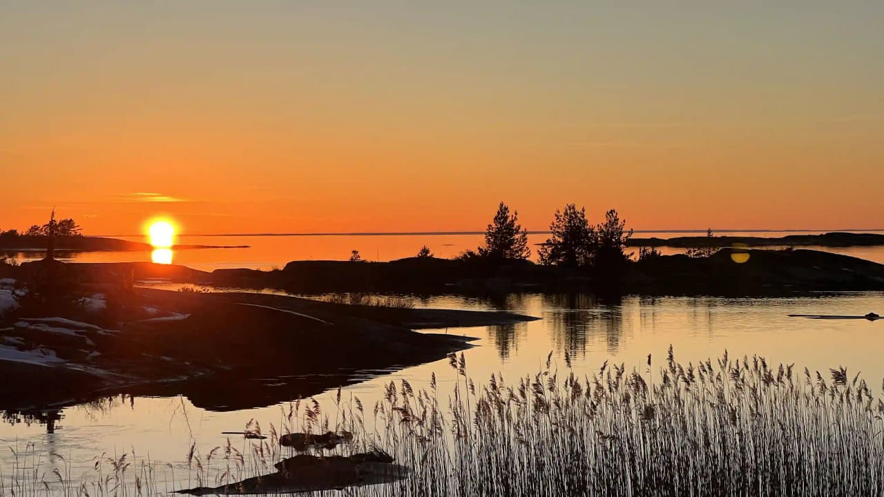 En vacker vy från Filsbäcks camping vid solnedgången, där himlen glöder i rödorange och speglas i det stilla vattnet.