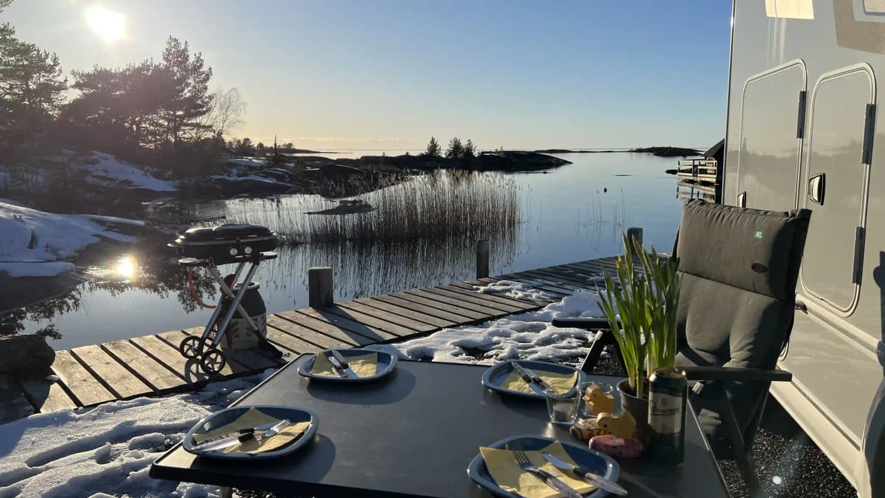 En motorbåt ligger förtöjd vid en småbåtshamn på Filsbäcks camping, med en glittrande sjö i bakgrunden och en grönskande omgivning.