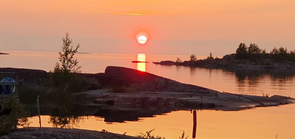 En vacker solnedgång vid Filsbäcks camping med en färgsprakande himmel i orange och rött över horisonten, vilket skapar en rofylld kvällsstämning vid kustlandskapet.