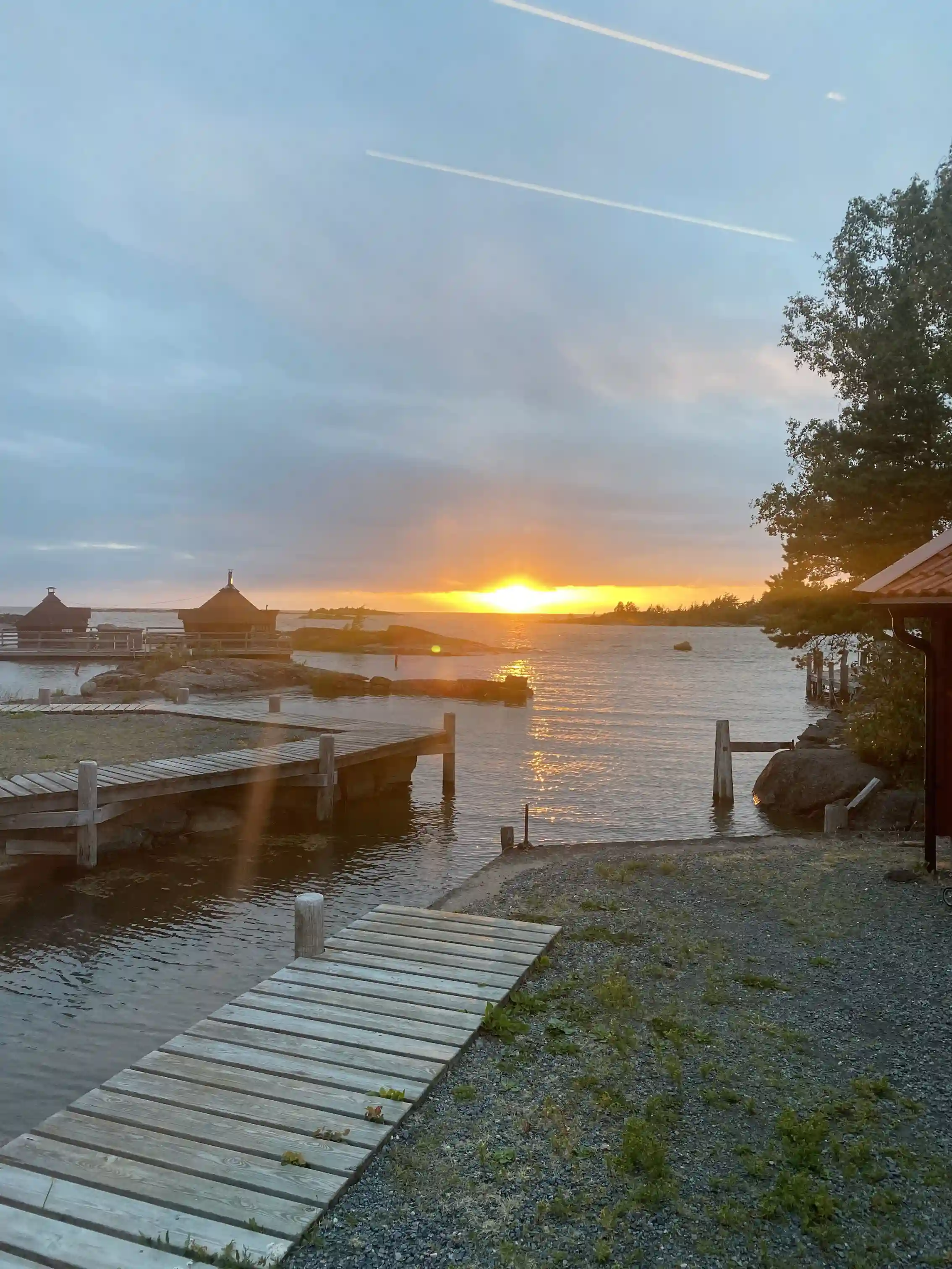 En stilla kvällsbild vid Filsbäcks camping med färgrik solnedgång över en sjö, där himlen speglas i vattnet. En brygga sträcker sig ut över sjön under den skymmande himlen med mjuka moln.