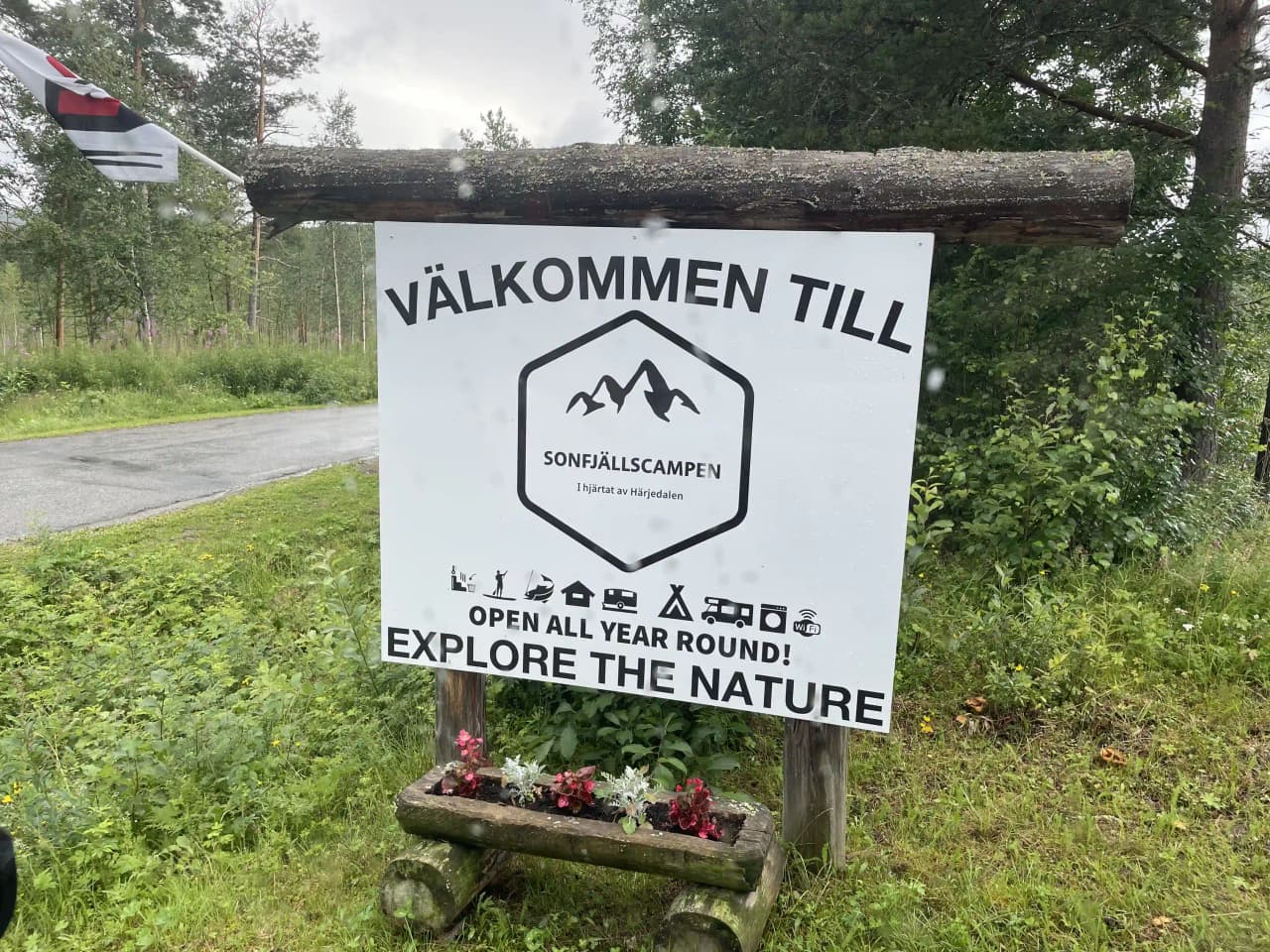 En skylt vid en grusväg i naturskön miljö visar vägen till Sonfjällscampen. Omgivningen präglas av tät grönska och en skogsstig syns i bakgrunden.