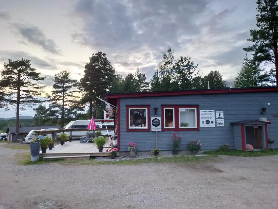 Alt-text: En stuga vid Sonfjällscampen med en asfalterad uppfart och grön gräsmatta runtomkring.