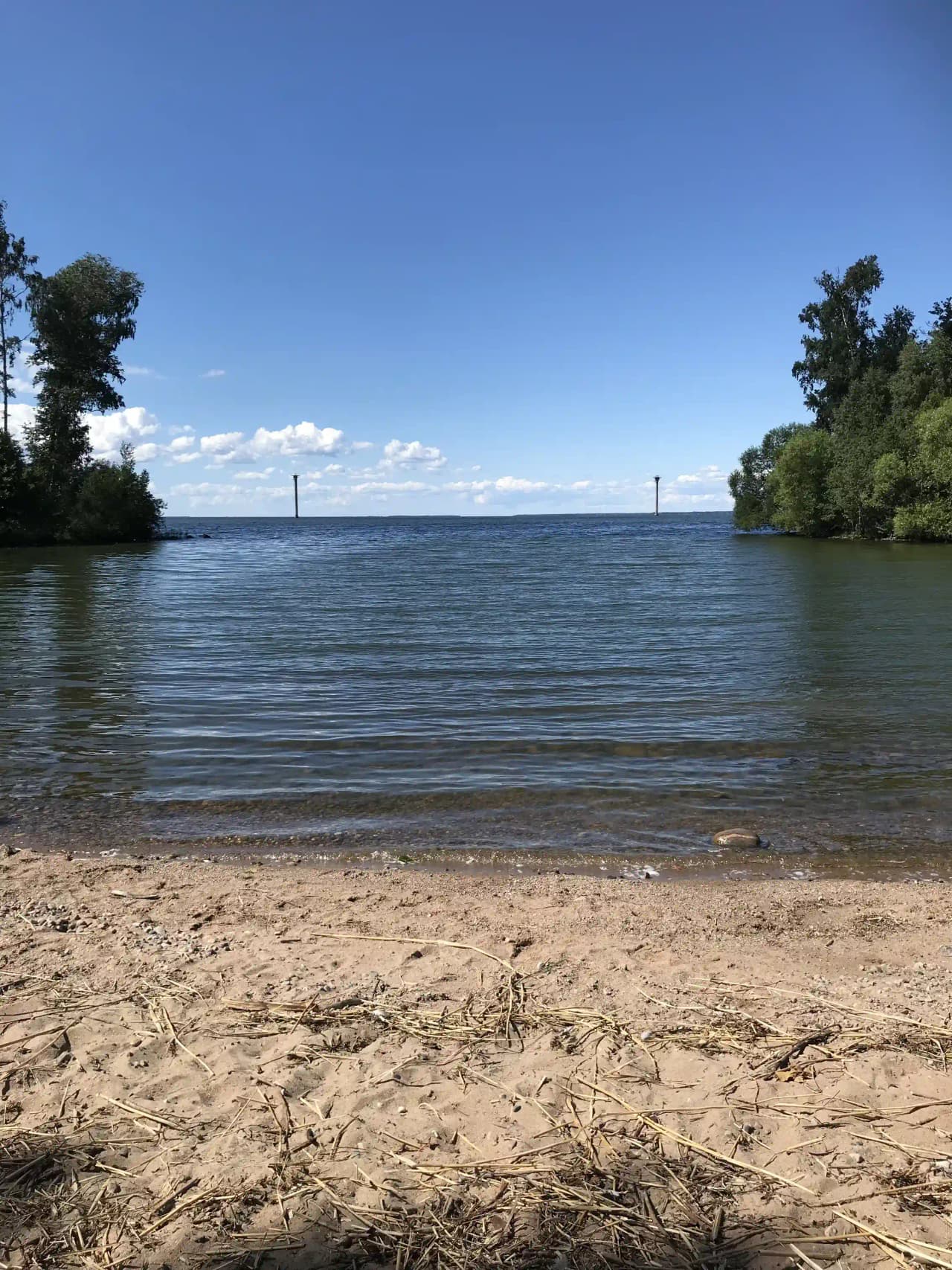 En naturskön vy vid Hjälmaresunds camping med utsikt över en stilla vattenyta och en vidsträckt blå himmel prydd med lätta moln.