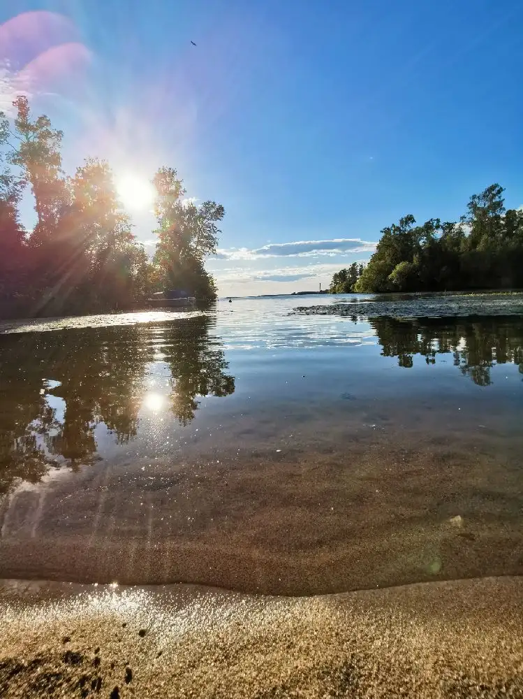 En vacker landskapsbild vid Hjälmaresunds camping med vidsträckt blå himmel och vatten, där molnen speglas på vattenytan i en stillsam och naturskön miljö.