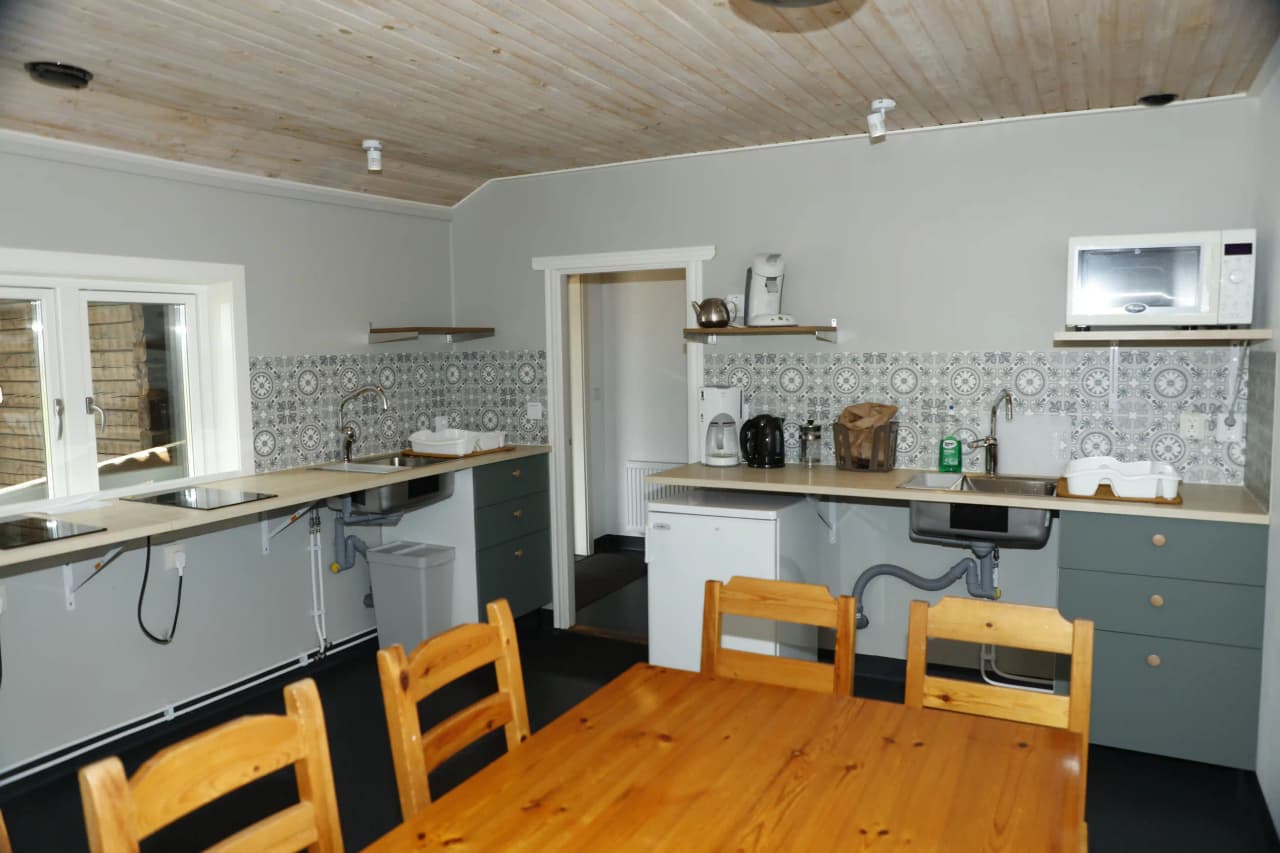 Alt-text: Interiörbild av ett kök på Våmåbadets camping, med trämöbler, trägolv och trädetaljer i taket. Köket är utrustat med bänkskiva och köksapparater samt en varm och inbjudande belysning.