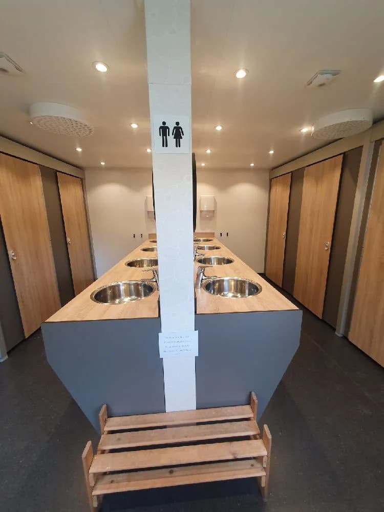 Interiörbild av Våmåbadets camping som visar ett rum med träinredning, golv och tak i trä. Belysning med silverfärgade armaturer.