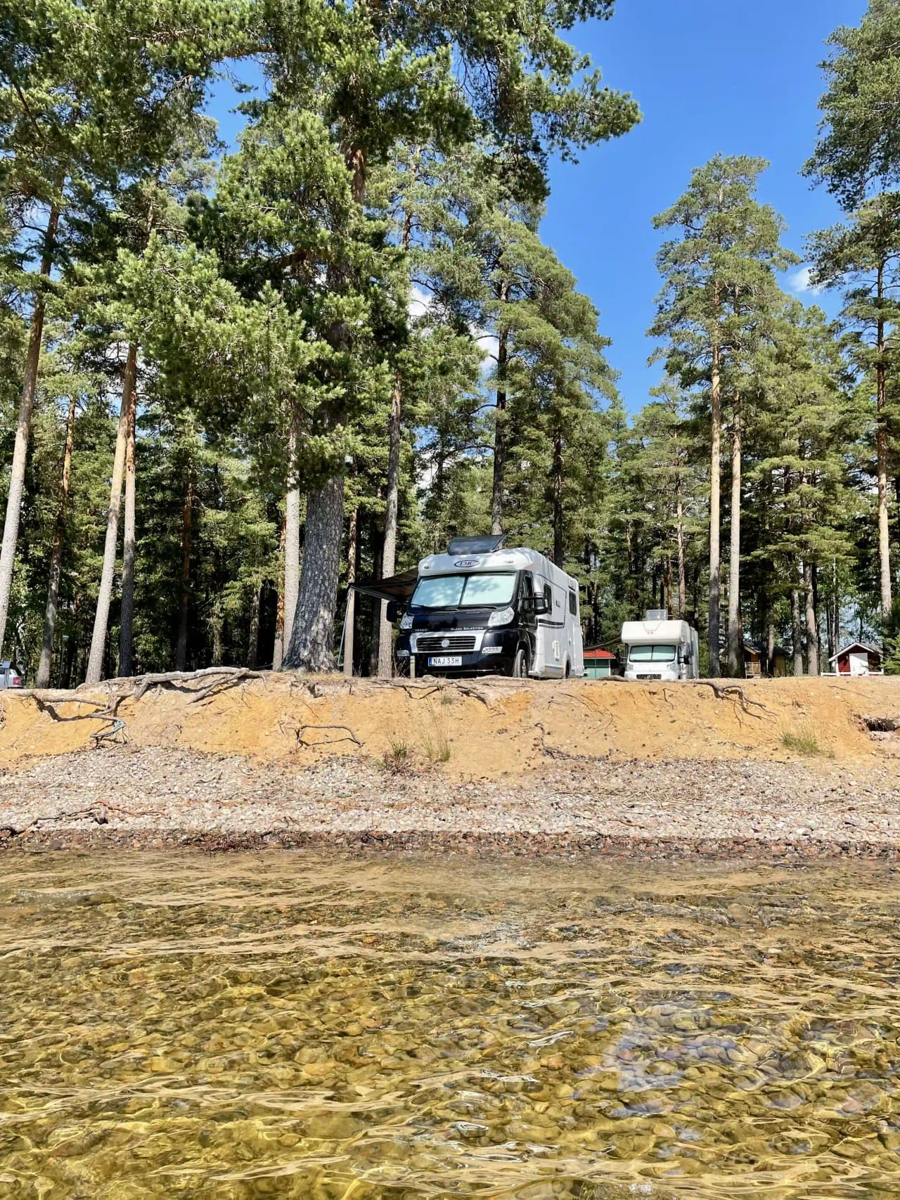 Alt-text: En husbil parkerad på Revelbadets camping med gröna omgivningar i bakgrunden.