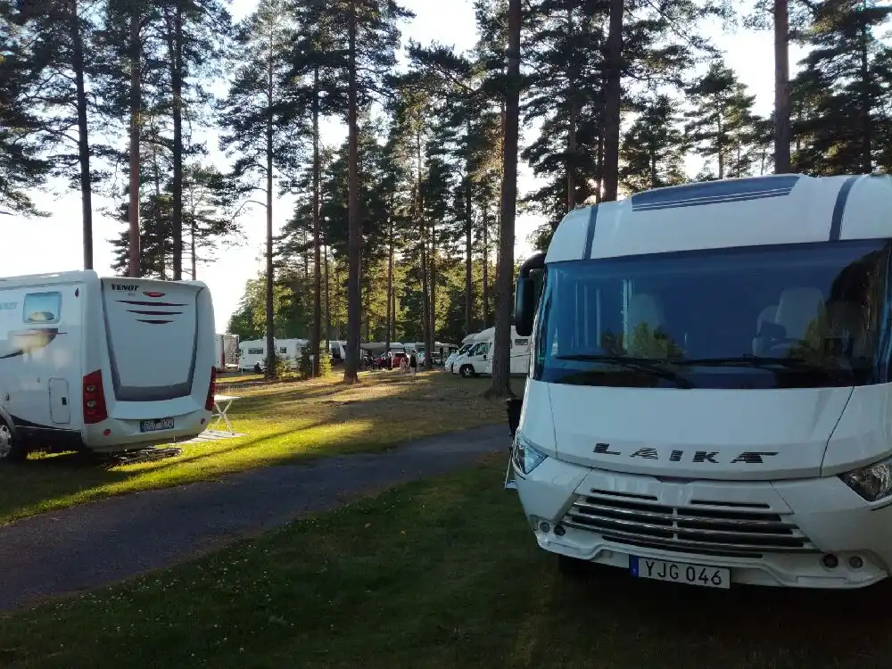 En husvagn parkerad på Revelbadets camping, omgiven av grönska. Fordonet syns tydligt med speglar, stötfångare och vindruta i fokus.