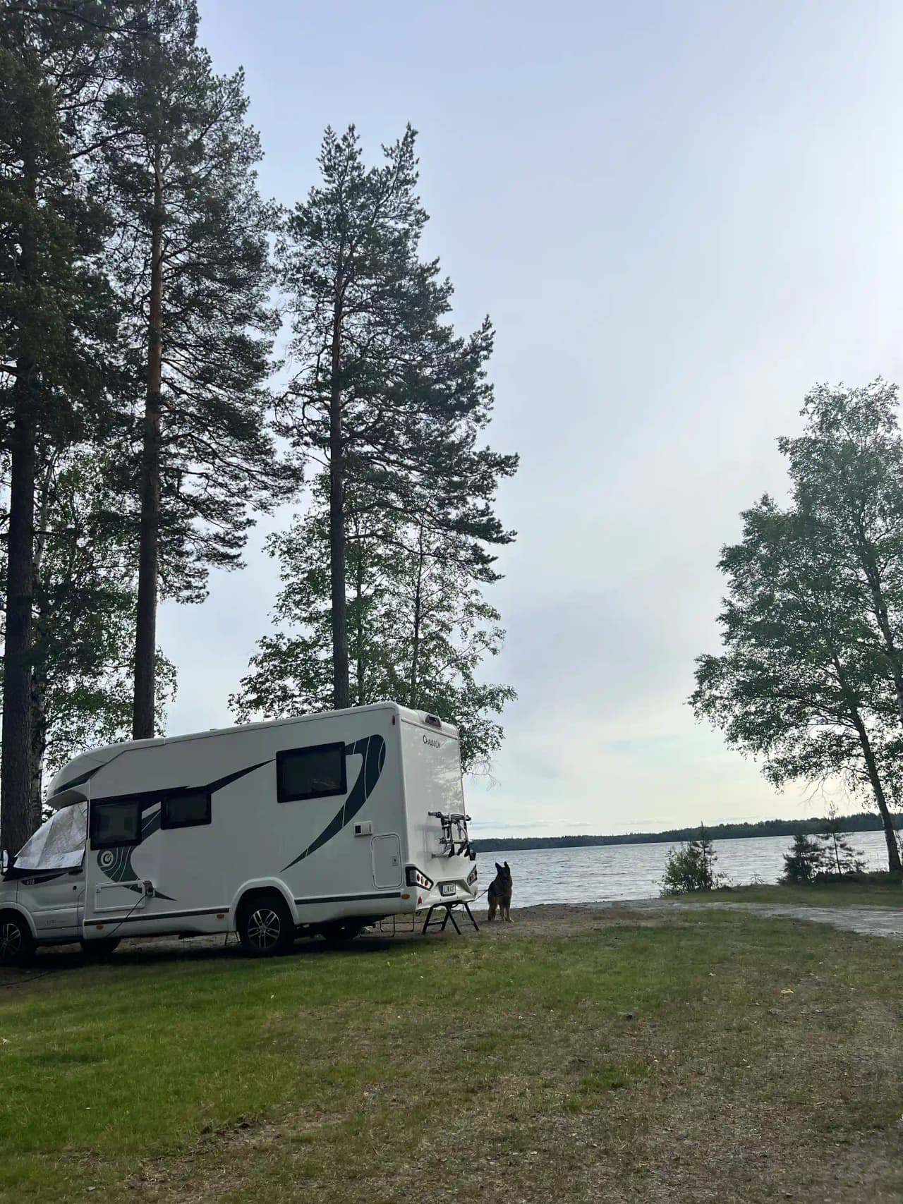 En campingplats med flera husvagnar och husbilar parkerade på Revelbadets camping. Området har öppna fält och är avsett för semestervistelser och friluftsliv.