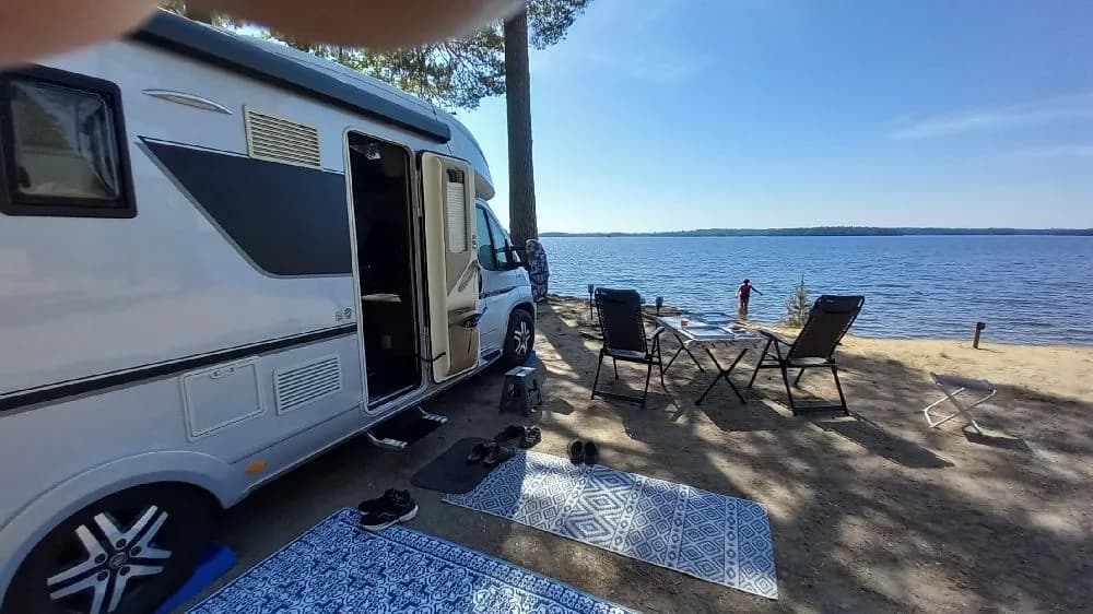En campingplats med flera husbilar och husvagnar parkerade bredvid varandra. På bilden syns även en båt och en cykel i närheten av campingfordonen, vilket antyder möjligheter till både vatten- och cykelaktiviteter.