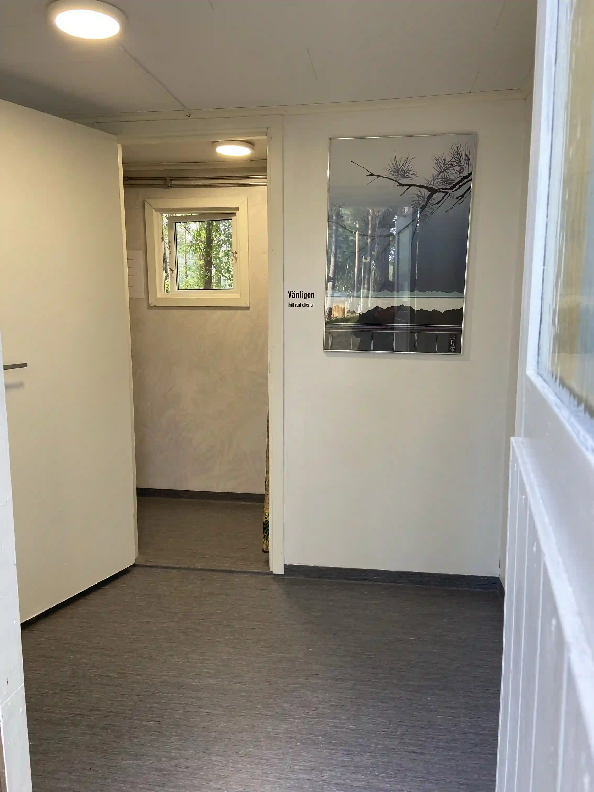 Ett interiörfoto av en träklädd campingsstuga på Revelbadets camping, med träväggar och trägolv samt en dörr och ett ljust tak.