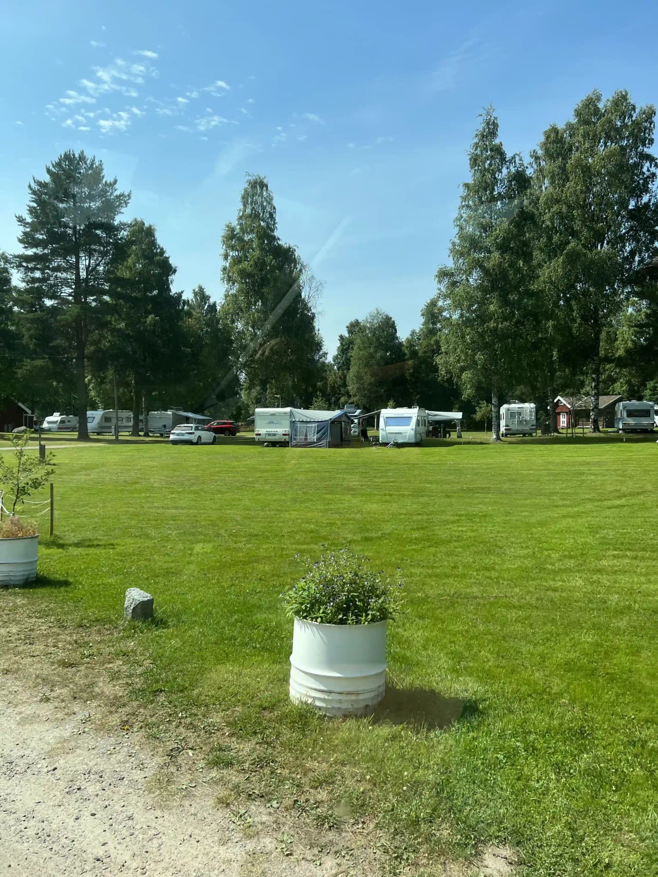 En campingplats vid Grebbestadfjorden med husvagnar uppställda på en grön gräsyta, omgiven av träd och molnigt väder.