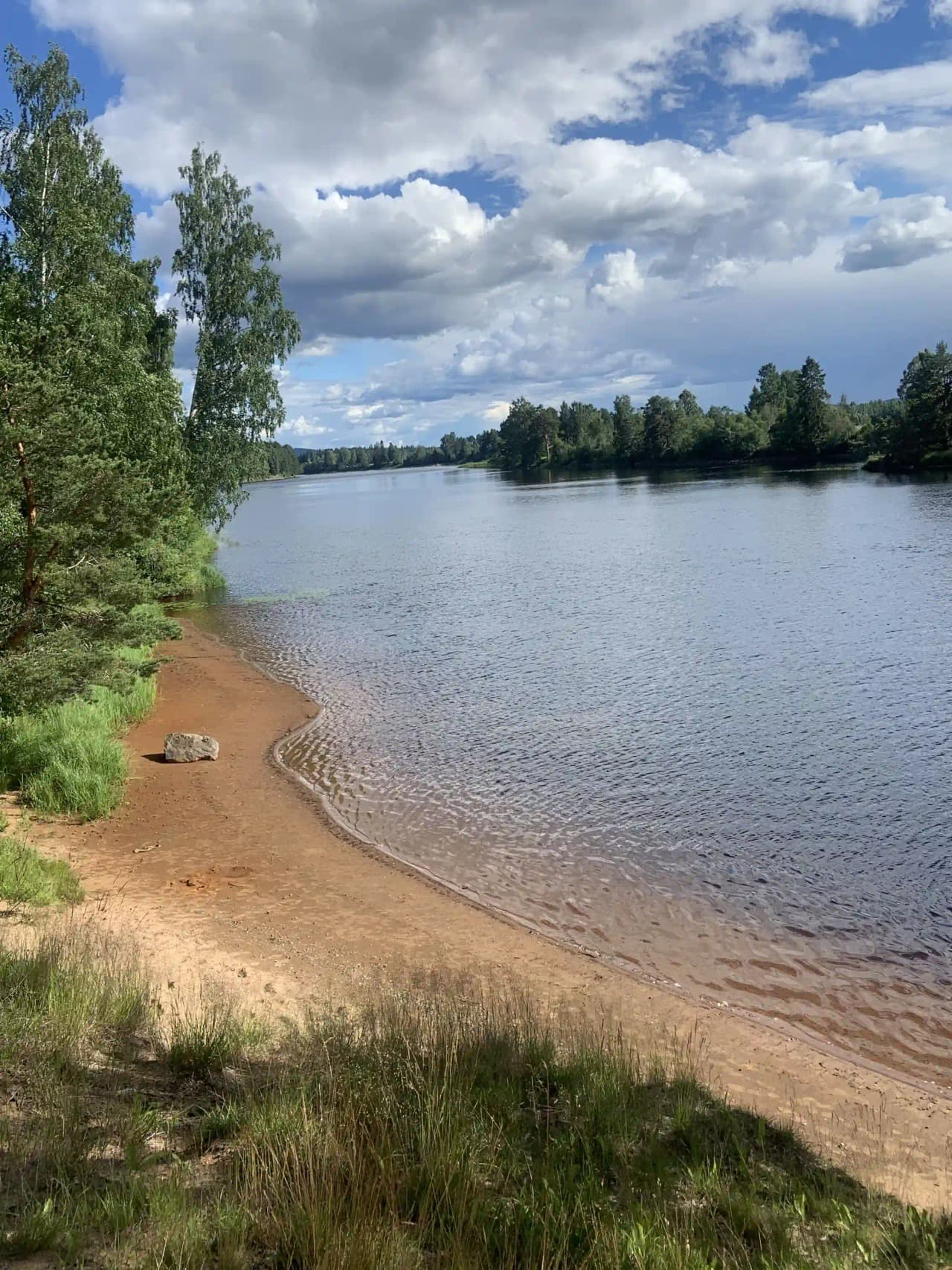 Vy över Nås camping med klarblå himmel, vattenresurs i förgrunden, omgiven av natur och vattenvägar.