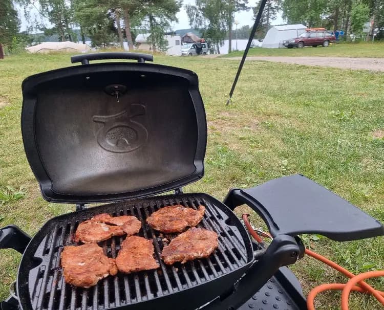 Bild av en utomhusgrill och kokredskap vid Vammervikens camping. Grillen är redo för matlagning i en naturskön campingmiljö.