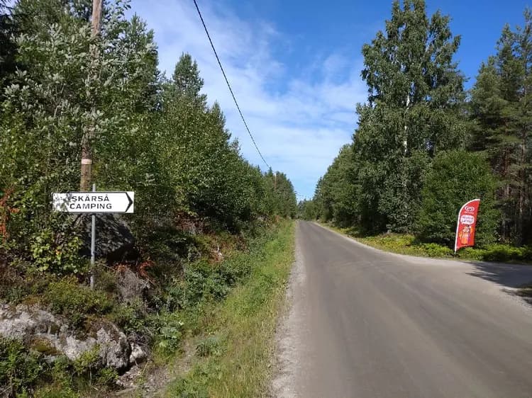 Alt-text: En landsväg omgiven av träd med en vägskylt som pekar mot Skärså Camping.