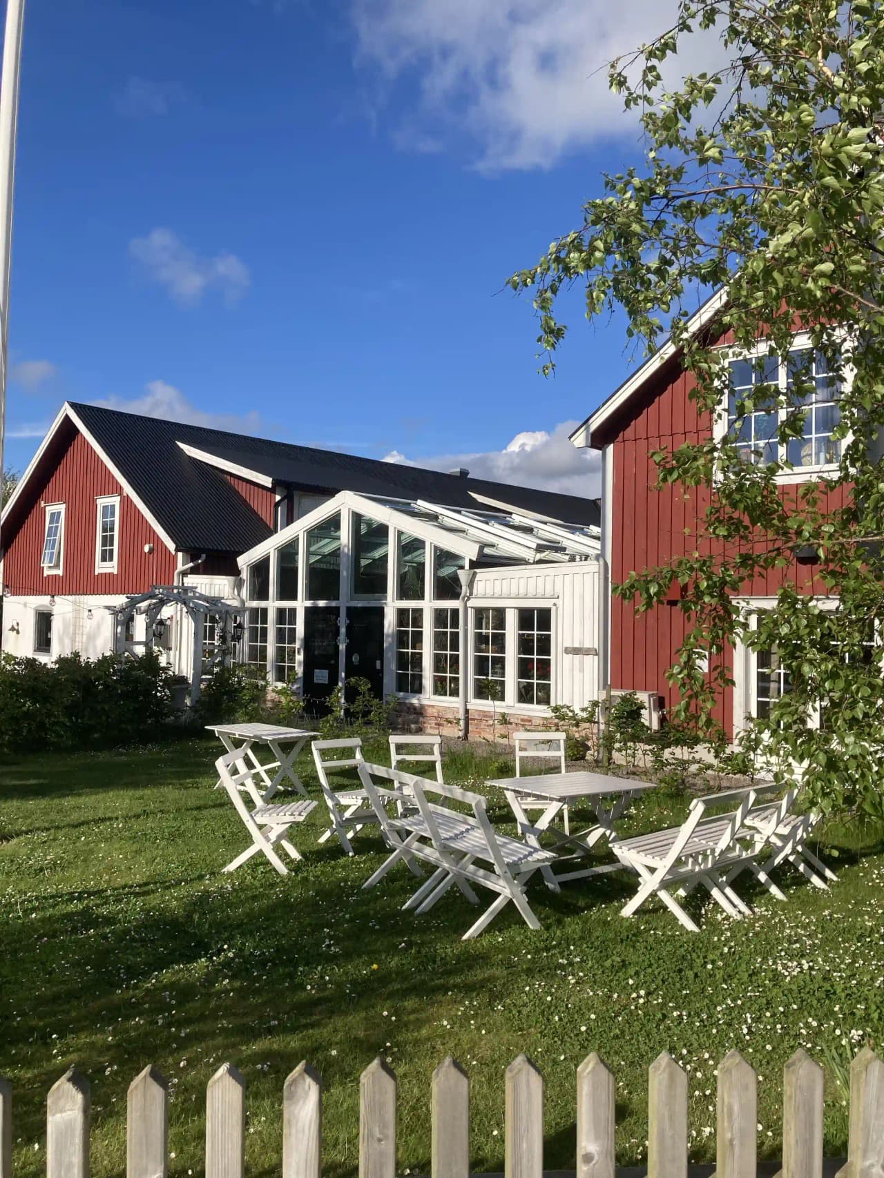 En lantlig gårdsmiljö med ett hotell och spa. Bilden visar en stuga omgiven av en grönskande trädgård med en välklippt gräsmatta och träd som skuggar området. Det finns också utemöbler placerade på gården.