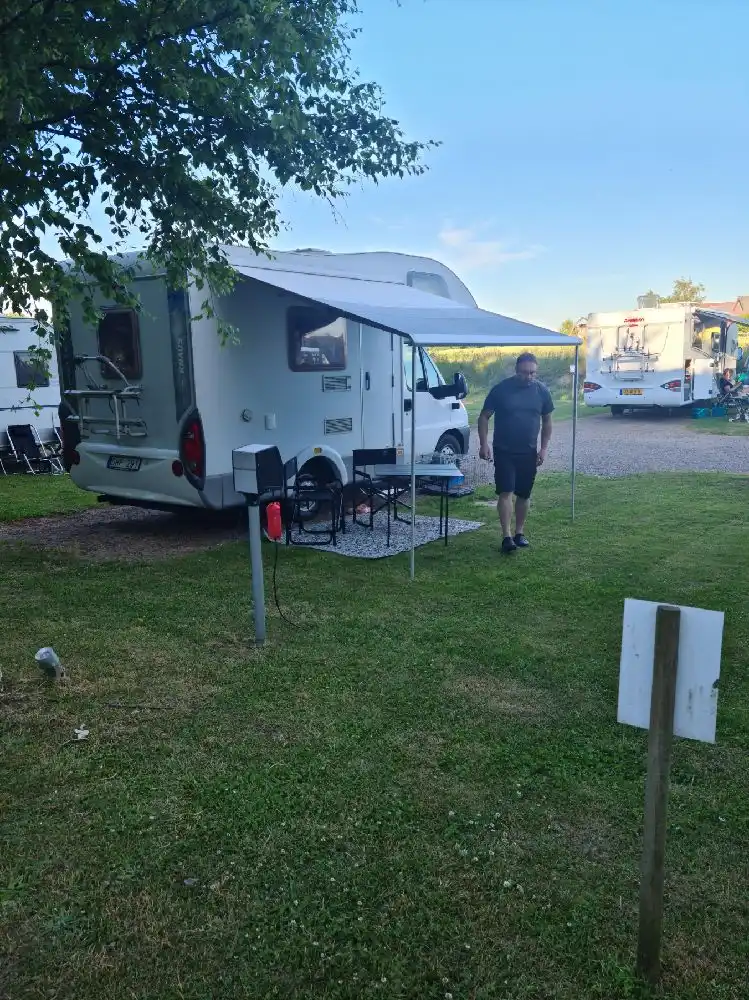 En campingplats vid Hotell & Spa Lögnäs Gård med husvagnar och tält parkerade i ett naturskönt område, omgivna av grönska och en avkopplande atmosfär.
